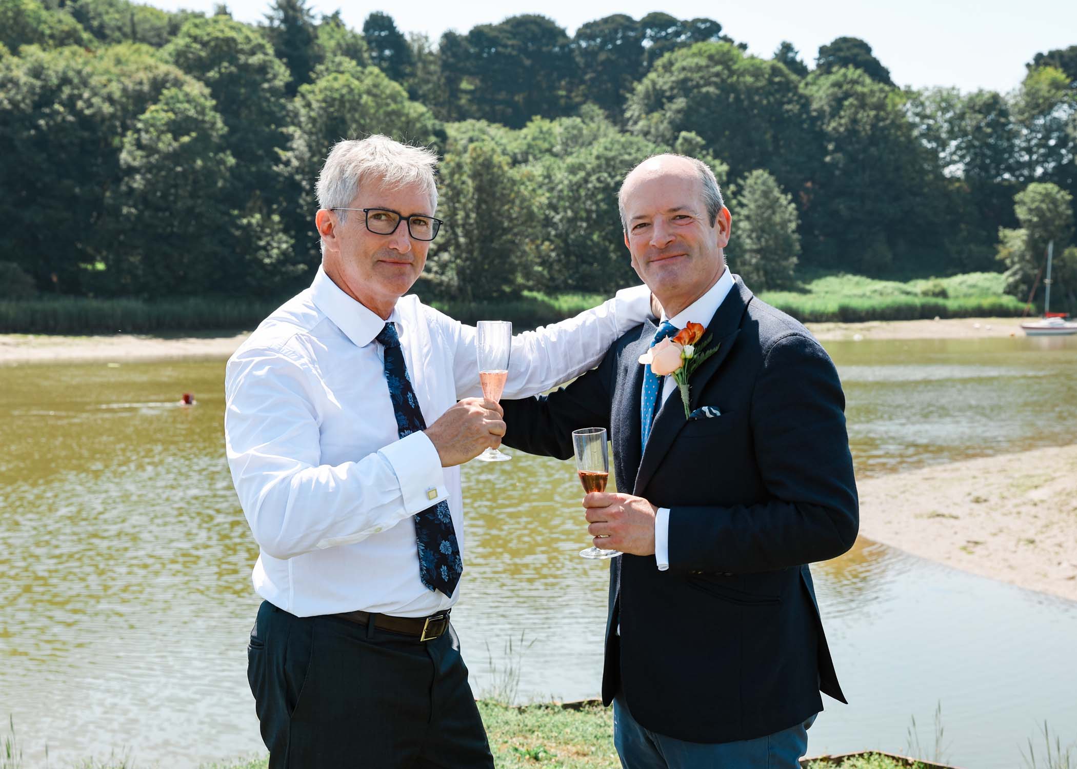A groom and his bestman cheersing on the penisula at woodbridge marina on a wedding day in Woodbridge captured by Suffolk Wedding Photographer Hayley Denston Photography